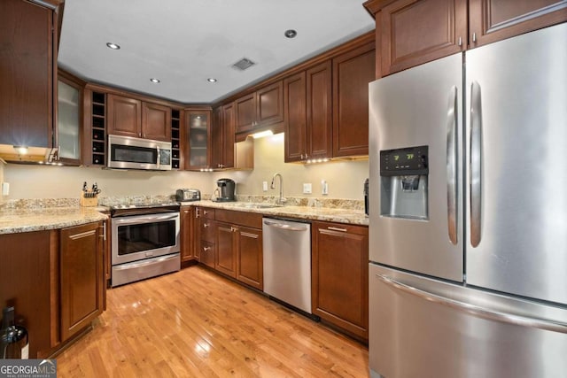 kitchen with light stone countertops, light wood-type flooring, sink, and appliances with stainless steel finishes