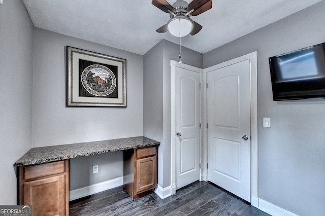 unfurnished office with ceiling fan, dark wood-type flooring, and built in desk