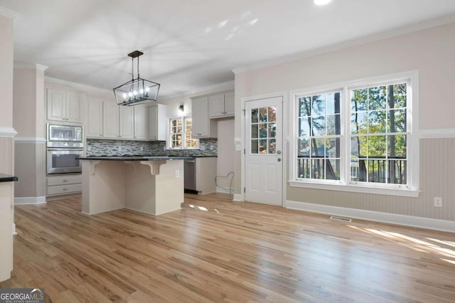 kitchen featuring white cabinets, hanging light fixtures, light hardwood / wood-style flooring, a kitchen bar, and stainless steel appliances