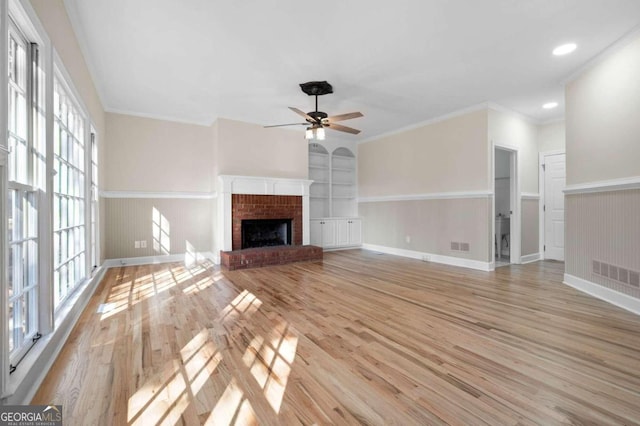 unfurnished living room featuring ceiling fan, built in features, crown molding, and light wood-type flooring