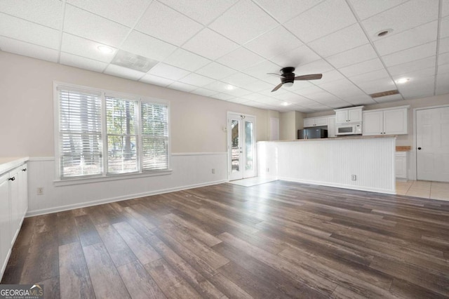 unfurnished living room featuring ceiling fan, a drop ceiling, and dark wood-type flooring