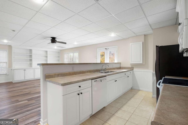 kitchen featuring white dishwasher, white cabinets, sink, built in shelves, and light wood-type flooring