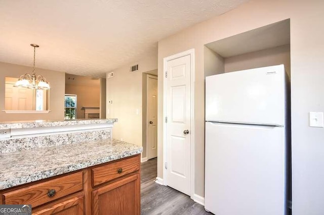 kitchen featuring light stone countertops, dark wood-type flooring, pendant lighting, white refrigerator, and an inviting chandelier