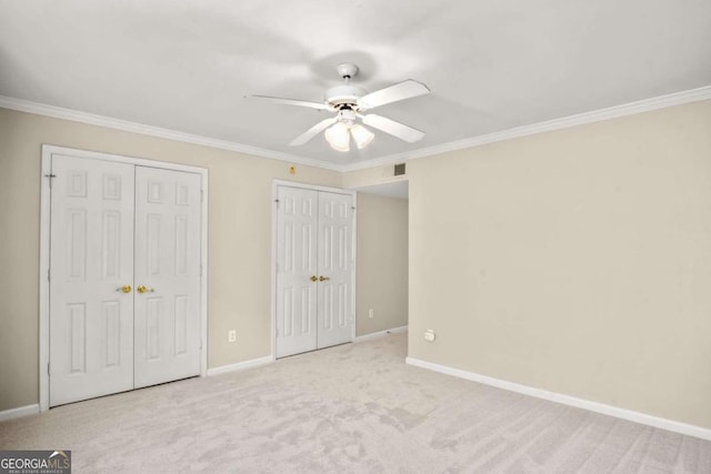 unfurnished bedroom with multiple closets, light carpet, crown molding, and ceiling fan