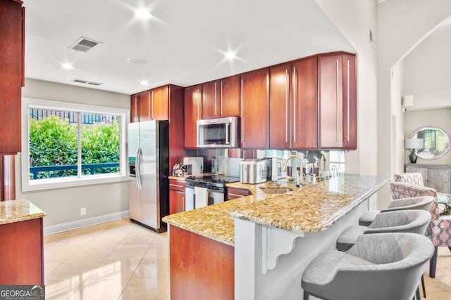 kitchen with kitchen peninsula, appliances with stainless steel finishes, light stone counters, light tile patterned floors, and a breakfast bar area