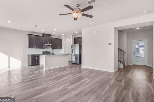 kitchen with ceiling fan, stainless steel appliances, an island with sink, light hardwood / wood-style floors, and dark brown cabinets