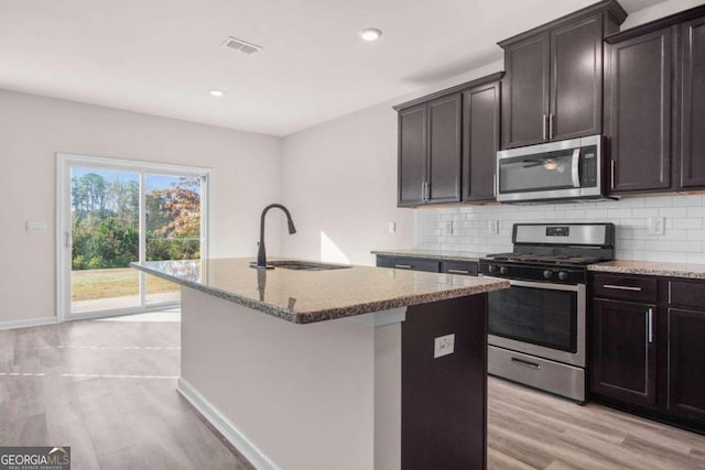 kitchen featuring a kitchen island with sink, sink, light hardwood / wood-style flooring, decorative backsplash, and appliances with stainless steel finishes