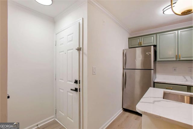 kitchen with stainless steel refrigerator, light stone counters, green cabinetry, light wood-type flooring, and ornamental molding