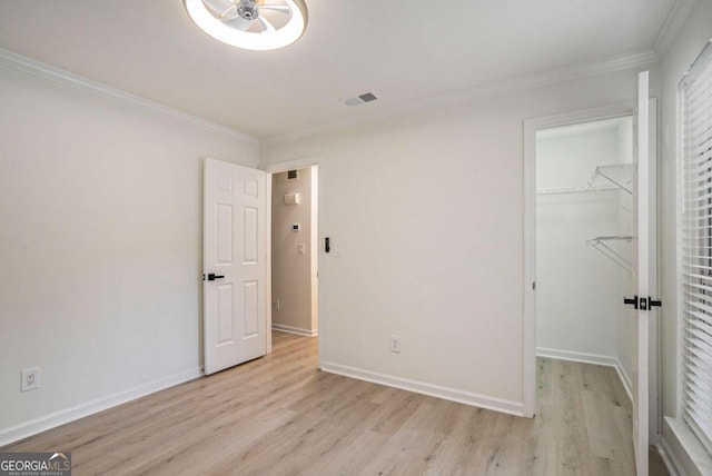 unfurnished bedroom featuring a walk in closet, crown molding, a closet, and light hardwood / wood-style flooring