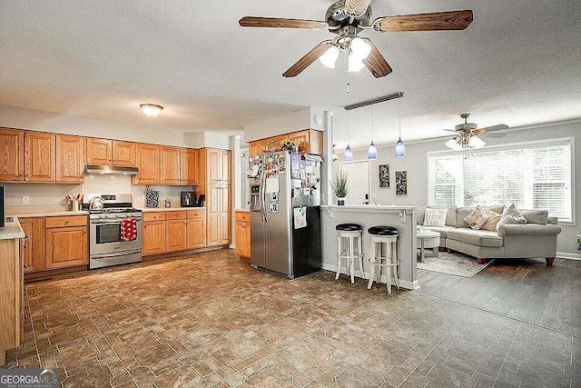 kitchen featuring a textured ceiling, a kitchen breakfast bar, hanging light fixtures, and appliances with stainless steel finishes