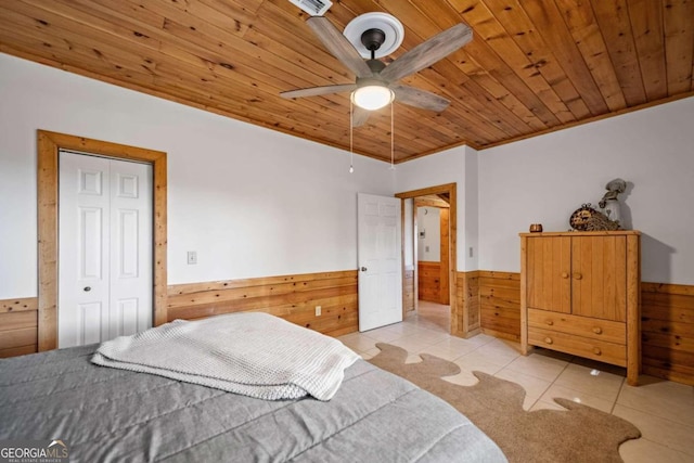 bedroom with ceiling fan, wooden ceiling, wood walls, a closet, and light tile patterned floors