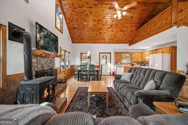 living room featuring light wood-type flooring, ceiling fan, high vaulted ceiling, wooden ceiling, and a wood stove