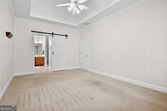 spare room with light carpet, ceiling fan, a barn door, ornamental molding, and a tray ceiling