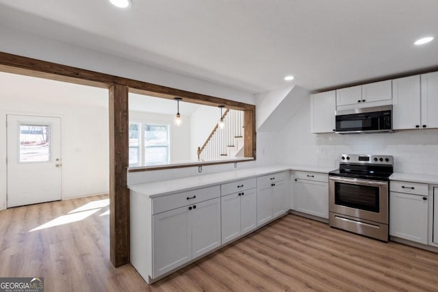 kitchen with white cabinets, appliances with stainless steel finishes, backsplash, and light hardwood / wood-style flooring