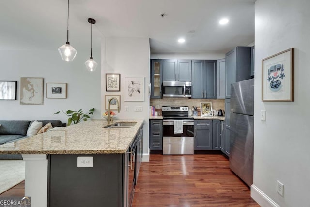 kitchen featuring appliances with stainless steel finishes, dark hardwood / wood-style flooring, light stone counters, sink, and pendant lighting