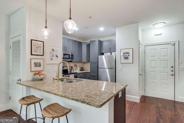 kitchen with sink, hanging light fixtures, stainless steel appliances, light stone counters, and kitchen peninsula