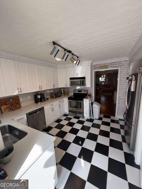 kitchen with ornamental molding, a textured ceiling, stainless steel appliances, sink, and white cabinets