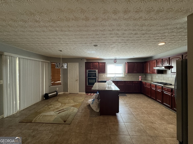 kitchen featuring a center island, backsplash, hanging light fixtures, a textured ceiling, and stainless steel appliances