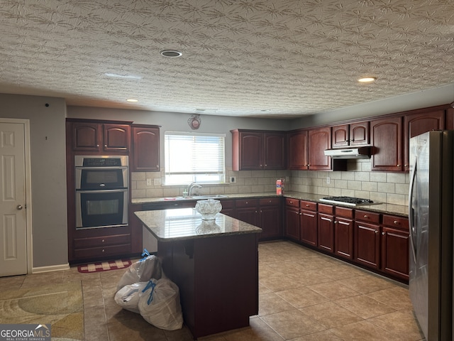 kitchen with light stone countertops, appliances with stainless steel finishes, tasteful backsplash, sink, and a center island