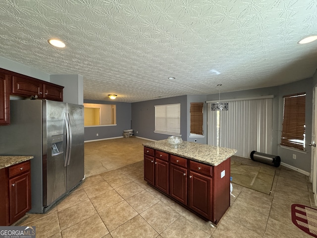 kitchen with stainless steel fridge, light stone counters, a textured ceiling, a kitchen island, and hanging light fixtures