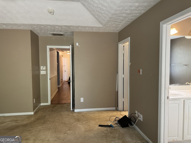 unfurnished bedroom featuring a textured ceiling, light colored carpet, and ensuite bath