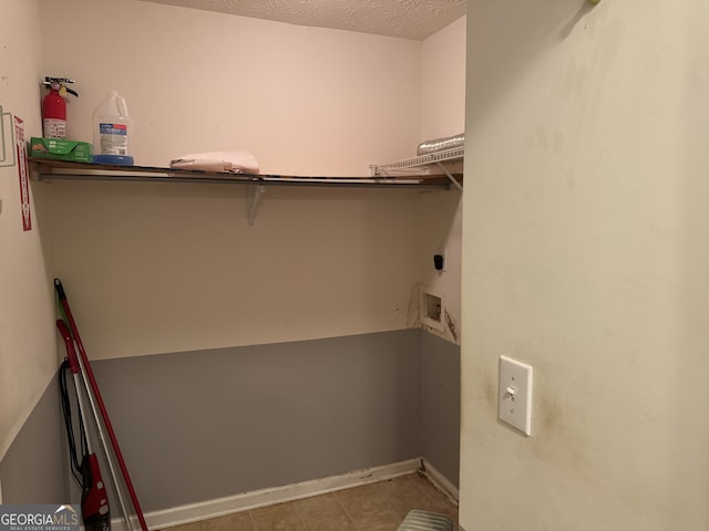 interior space with electric dryer hookup, light tile patterned floors, a textured ceiling, and hookup for a washing machine