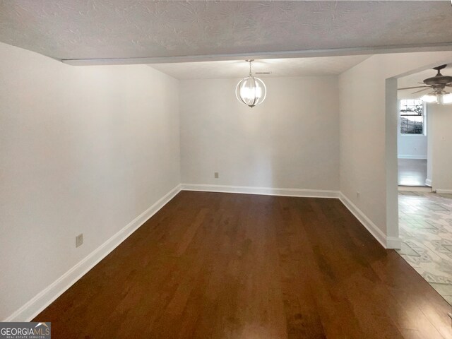 unfurnished room with a textured ceiling, ceiling fan with notable chandelier, and dark wood-type flooring