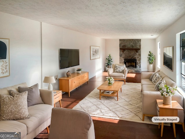 living room with a textured ceiling, dark hardwood / wood-style floors, and a stone fireplace