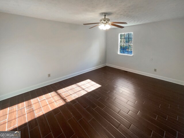 empty room featuring ceiling fan, dark wood-type flooring, and a textured ceiling