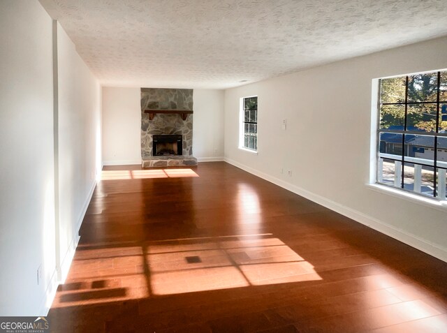 unfurnished living room featuring a stone fireplace, a textured ceiling, and hardwood / wood-style flooring