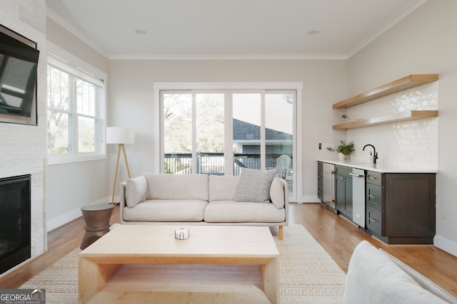 living room featuring indoor wet bar, ornamental molding, a fireplace, and light hardwood / wood-style flooring