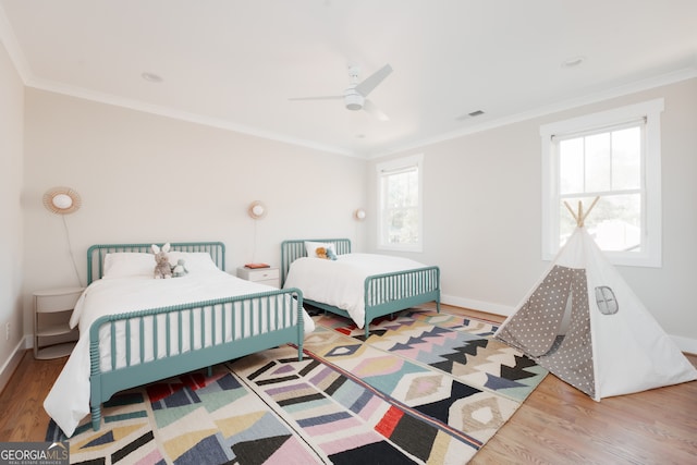 bedroom featuring ceiling fan, light wood-type flooring, ornamental molding, and multiple windows