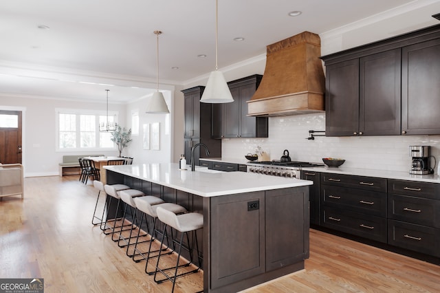 kitchen with a kitchen breakfast bar, an island with sink, pendant lighting, light hardwood / wood-style floors, and custom range hood