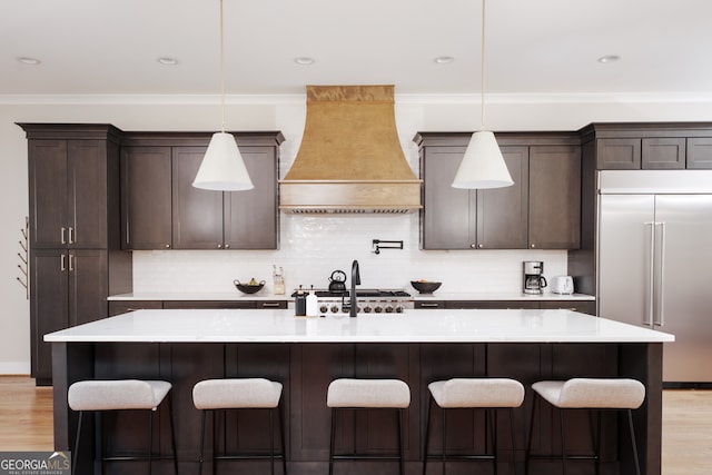 kitchen featuring hanging light fixtures, custom range hood, appliances with stainless steel finishes, and a kitchen island with sink