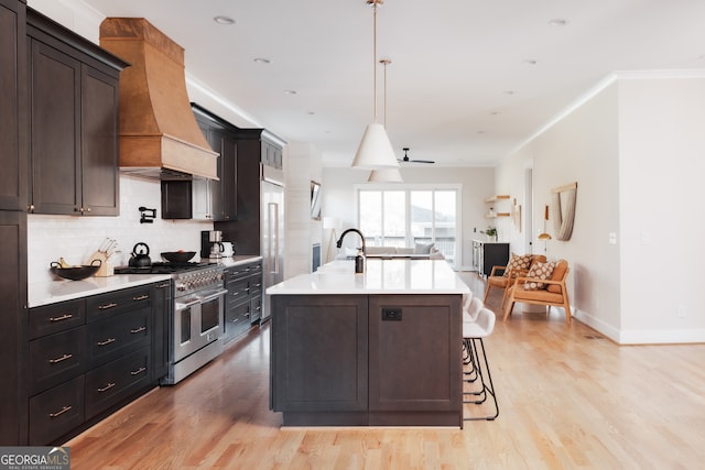 kitchen featuring ornamental molding, a center island with sink, double oven range, light hardwood / wood-style floors, and hanging light fixtures