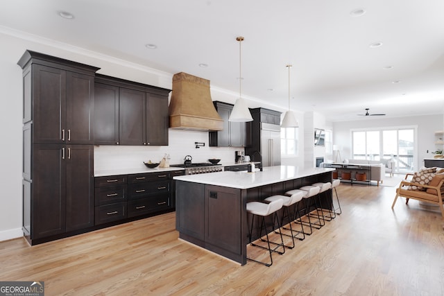 kitchen featuring ceiling fan, a kitchen breakfast bar, an island with sink, pendant lighting, and custom exhaust hood