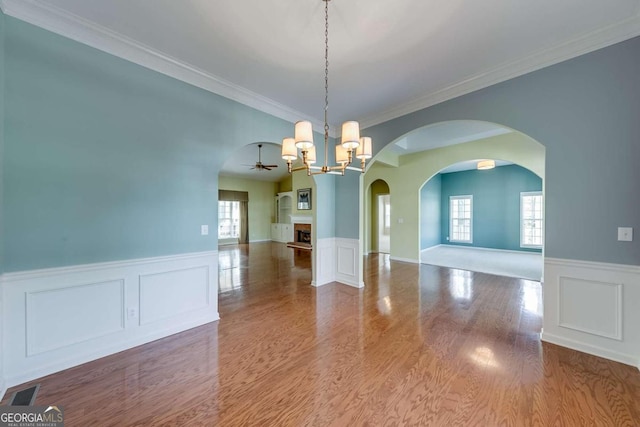 unfurnished dining area featuring ornamental molding, ceiling fan with notable chandelier, and hardwood / wood-style flooring