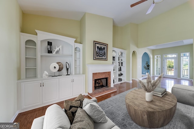 living room with dark hardwood / wood-style flooring, a brick fireplace, ceiling fan, and a high ceiling