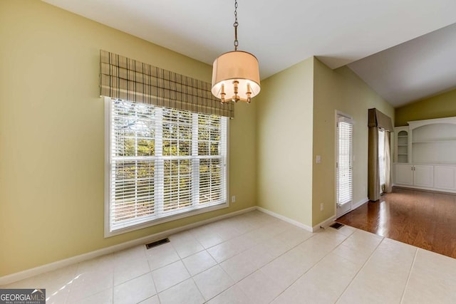 unfurnished dining area with lofted ceiling, built in features, light tile patterned floors, and an inviting chandelier