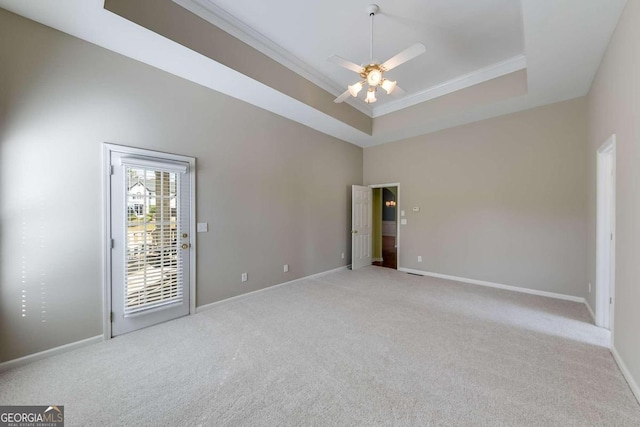 empty room with a tray ceiling, ceiling fan, light colored carpet, and ornamental molding