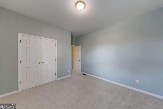 unfurnished bedroom with light colored carpet and a closet