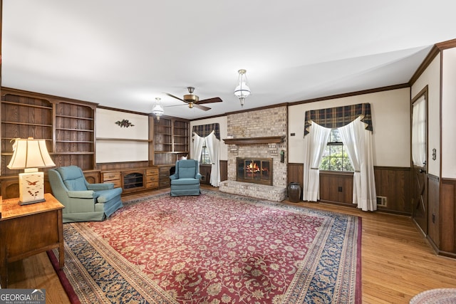 living room featuring wood walls, crown molding, a brick fireplace, ceiling fan, and light hardwood / wood-style floors