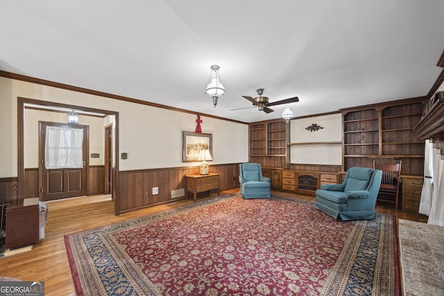 sitting room featuring ceiling fan, built in features, crown molding, wood walls, and light wood-type flooring