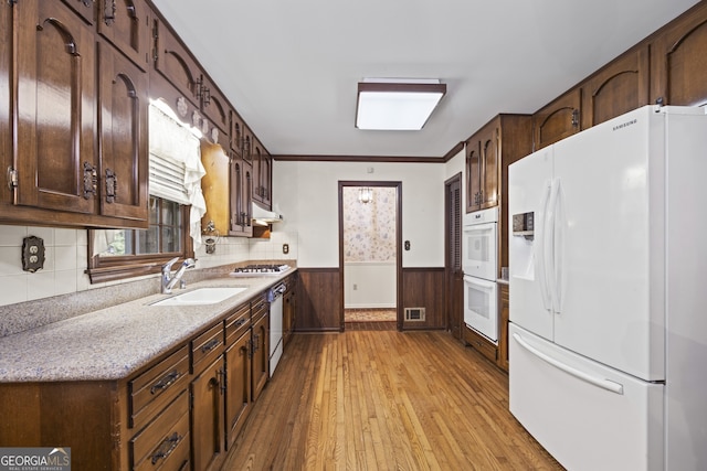 kitchen featuring white appliances, sink, wooden walls, light wood-type flooring, and ornamental molding