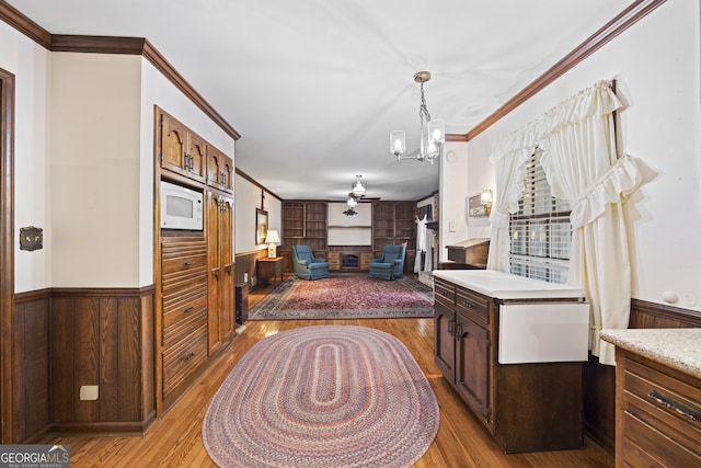 kitchen with ceiling fan with notable chandelier, crown molding, wooden walls, and light hardwood / wood-style flooring