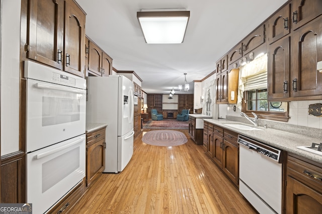 kitchen featuring sink, hanging light fixtures, light hardwood / wood-style flooring, a chandelier, and white appliances