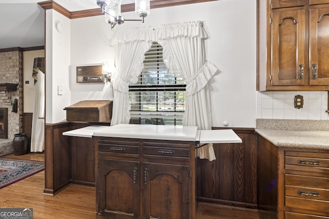 kitchen with crown molding, light hardwood / wood-style flooring, a fireplace, tasteful backsplash, and a chandelier