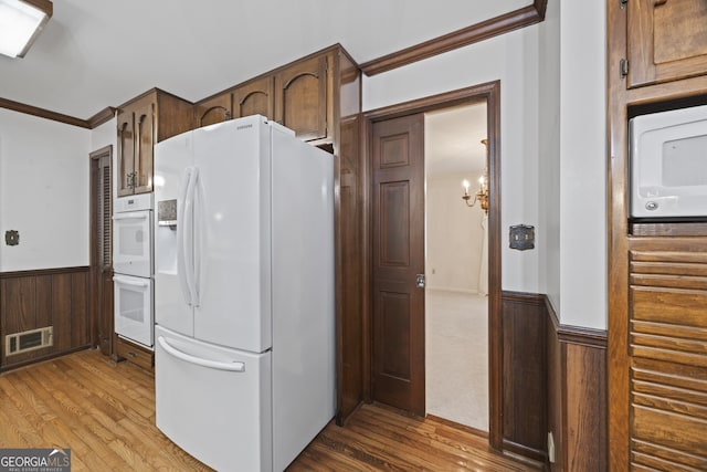 kitchen with light hardwood / wood-style flooring, a notable chandelier, white appliances, wooden walls, and ornamental molding