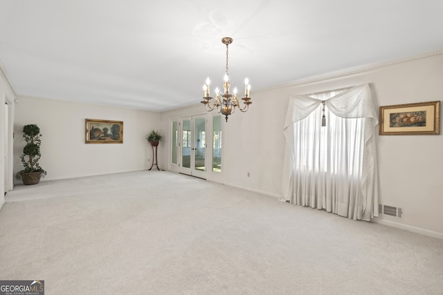 spare room featuring light carpet, ornamental molding, and an inviting chandelier