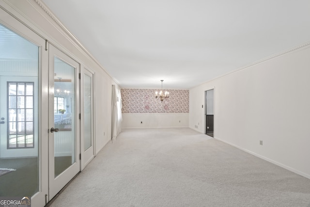 carpeted empty room with french doors, a chandelier, and ornamental molding